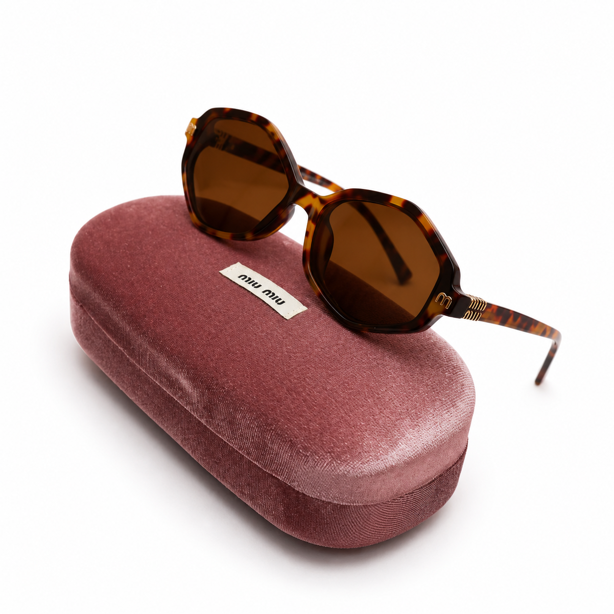 Miu Miu geometric octagonal sunglasses in tortoise shell with brown lenses, displayed on dusty rose velvet Miu Miu case